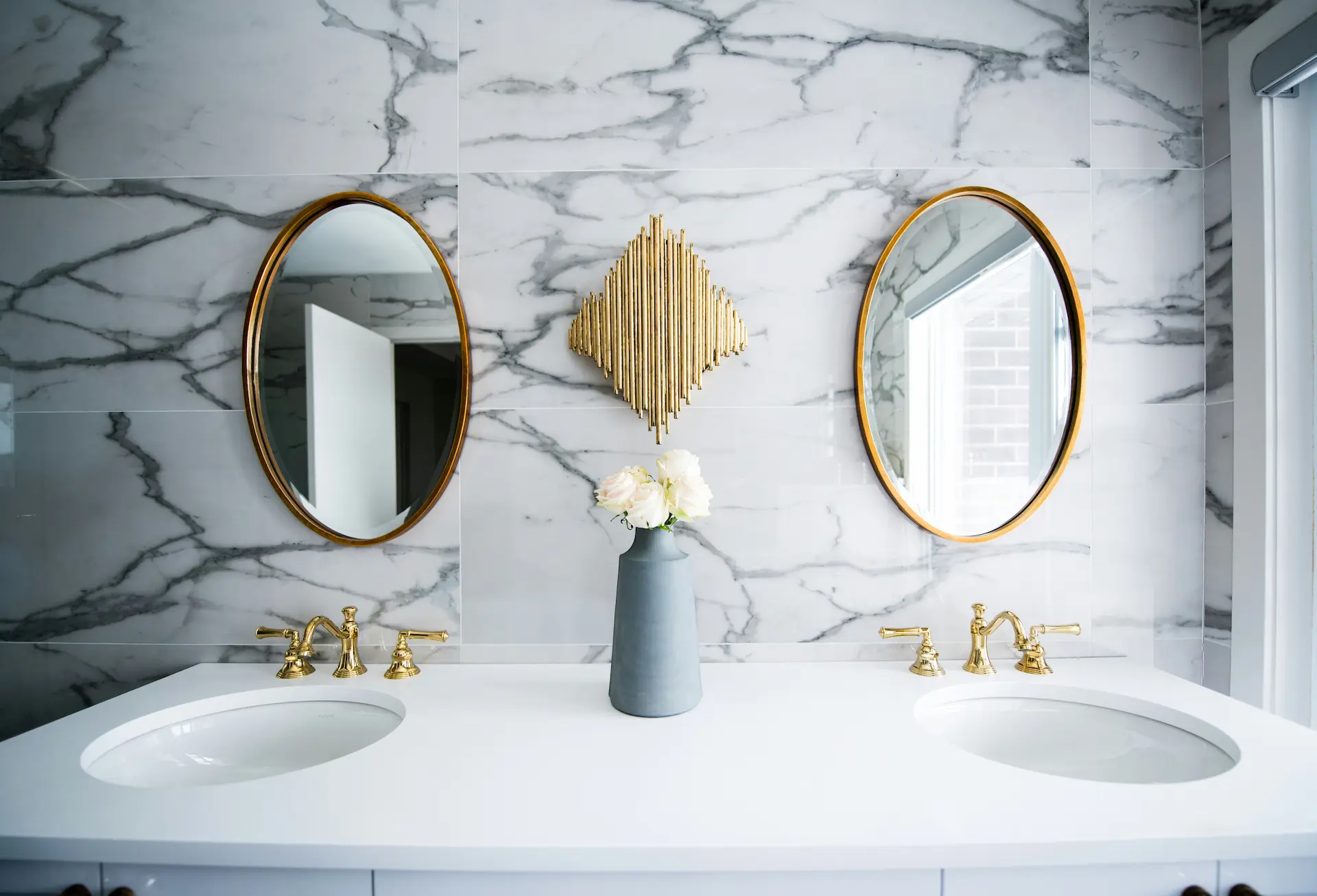 Luxurious bathroom design featuring a dual sink vanity with gold faucets, oval mirrors, and a marble-patterned PVC sheet by Milago Design, part of Milano Pergola Systems.