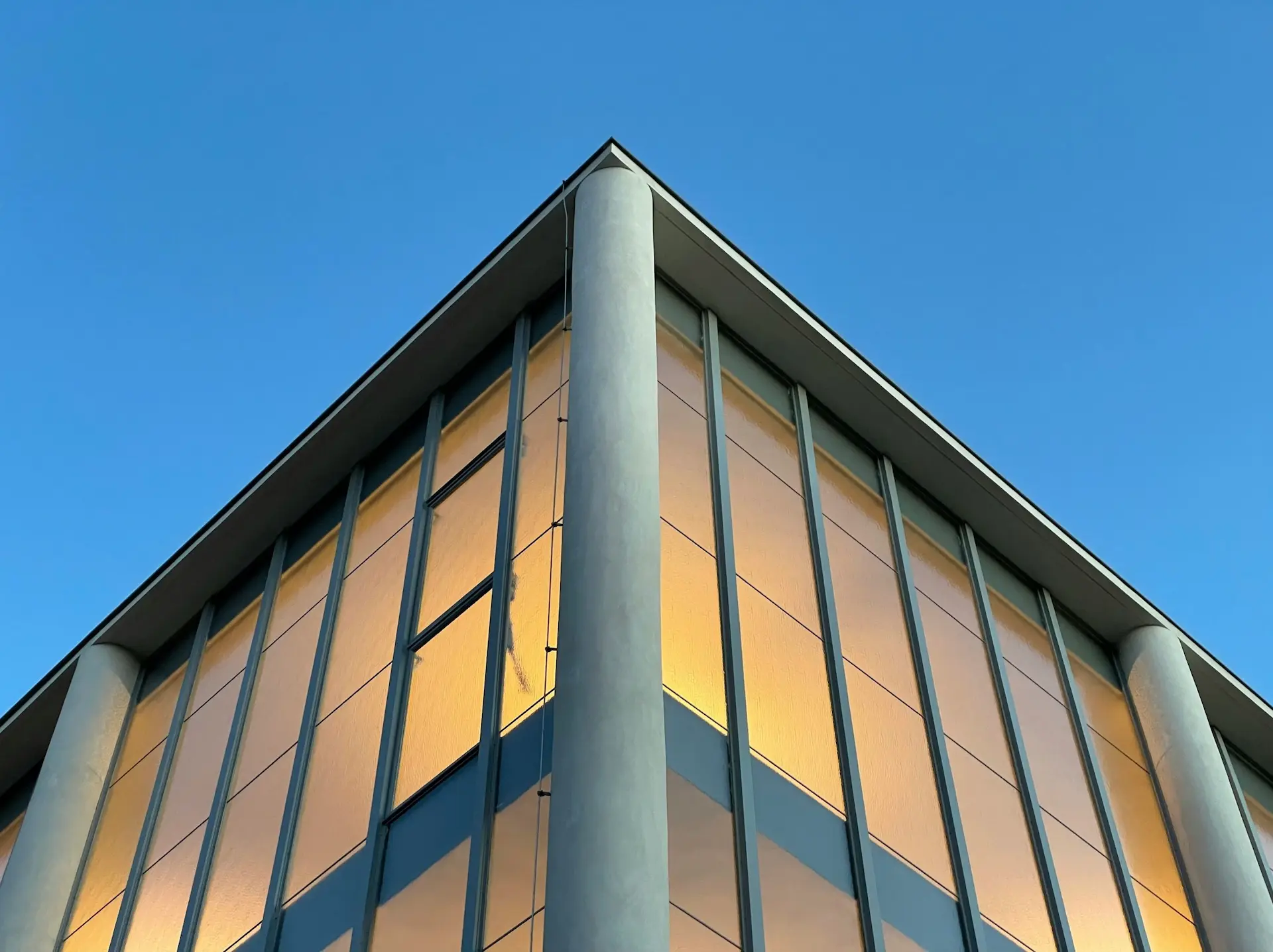 Modern building facade with large safety glass panels reflecting warm light, designed by Milago Design, part of Milano Pergola Systems.